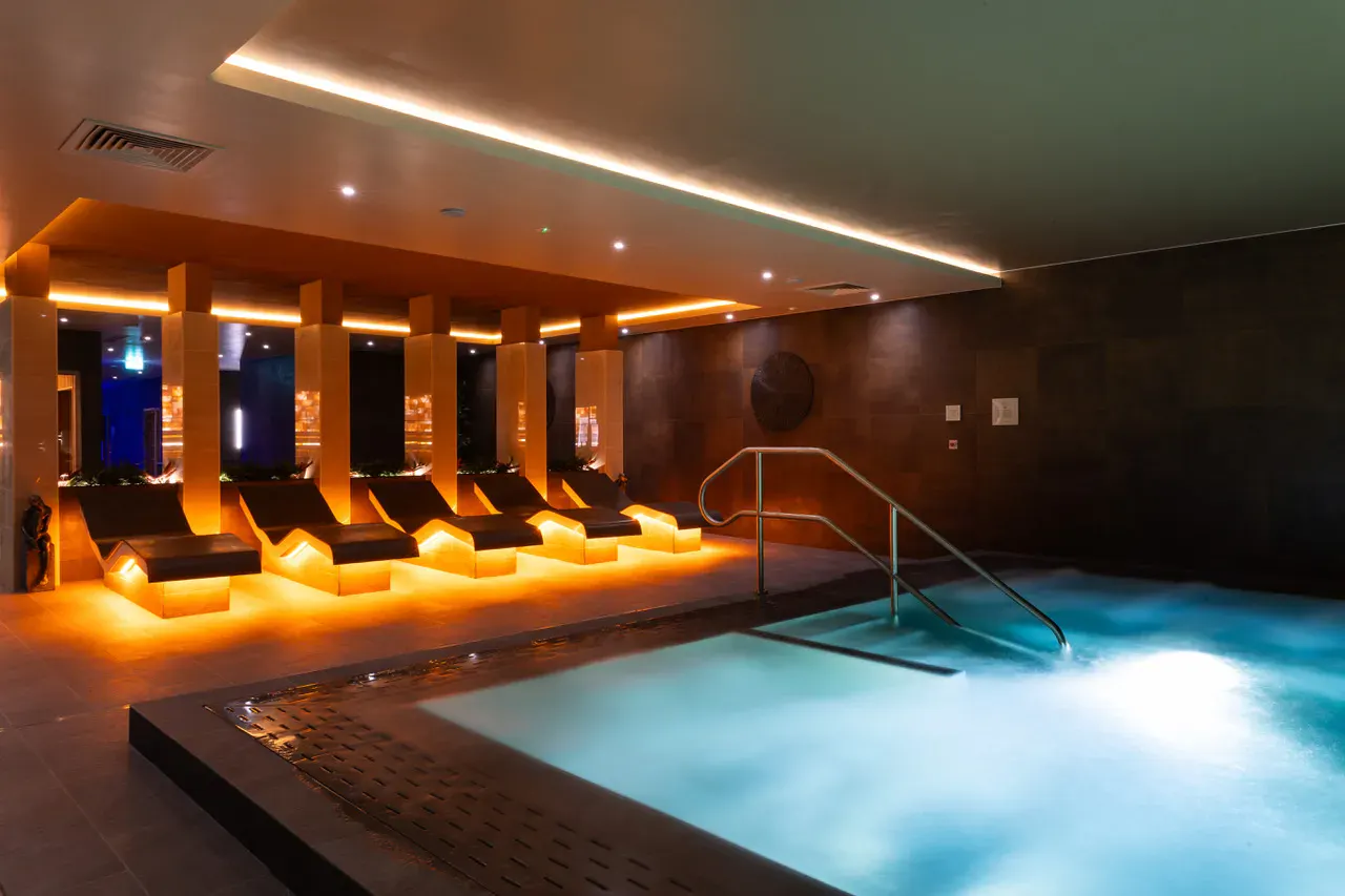 Luxury indoor hydrotherapy pool and heated relaxation loungers with warm mood lighting at David Lloyd St Neots spa facility.